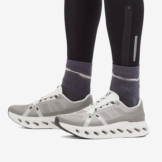 Gray athletic sneakers with a perforated, sculpted white sole, worn with purple tie-dye socks and black leggings with a zipper pocket.