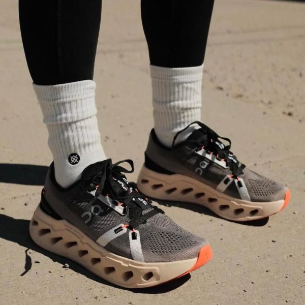 Gray athletic running shoes with breathable mesh, black accents, and orange-tipped soles worn with white crew socks on pavement.