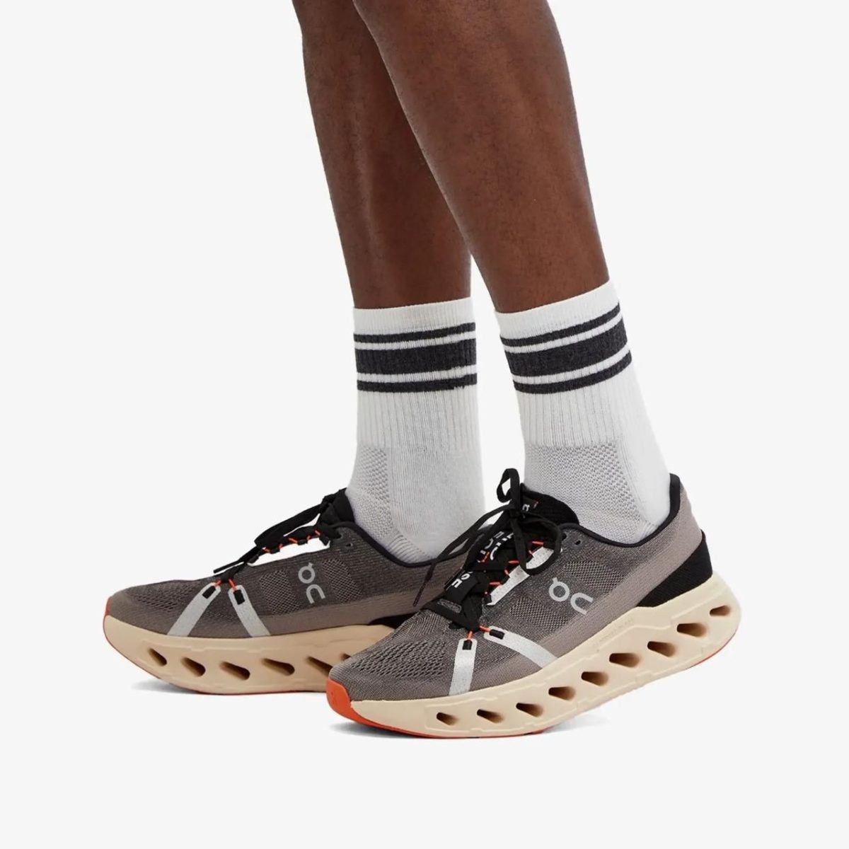 Person wearing white crew socks with two black stripes, standing in gray On running shoes with a tan hollow-sole midsole.