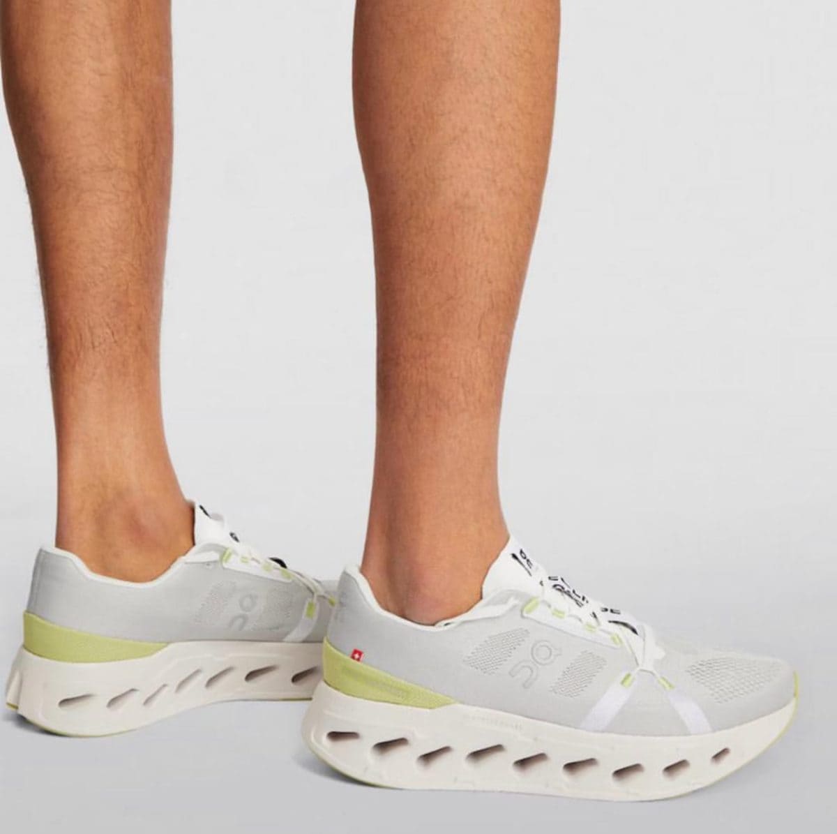 White and light gray running sneakers with lime accents and a hollow-cut sole worn on feet