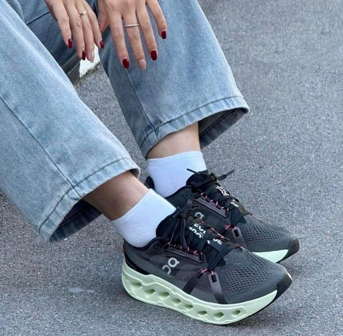 Close-up of feet in dark athletic sneakers with a mint-green chunky sole, white socks, and cuffed light-wash jeans.