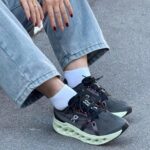 Close-up of feet in dark athletic sneakers with a mint-green chunky sole, white socks, and cuffed light-wash jeans.