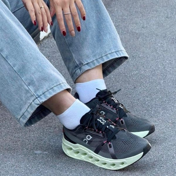 Close-up of feet in dark athletic sneakers with a mint-green chunky sole, white socks, and cuffed light-wash jeans.