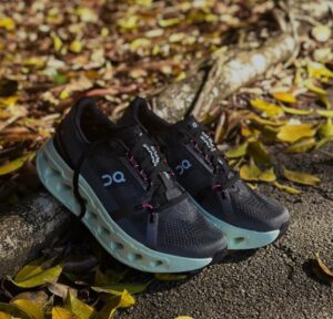 WhatsApp_Image_2025-01-19_at_11.59.14 | UAE SPORT STORE Pair of black running shoes with thick light-blue soles resting on a curb among fallen autumn leaves.