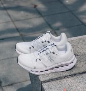Pair of white running shoes resting on a concrete ledge outdoors.
