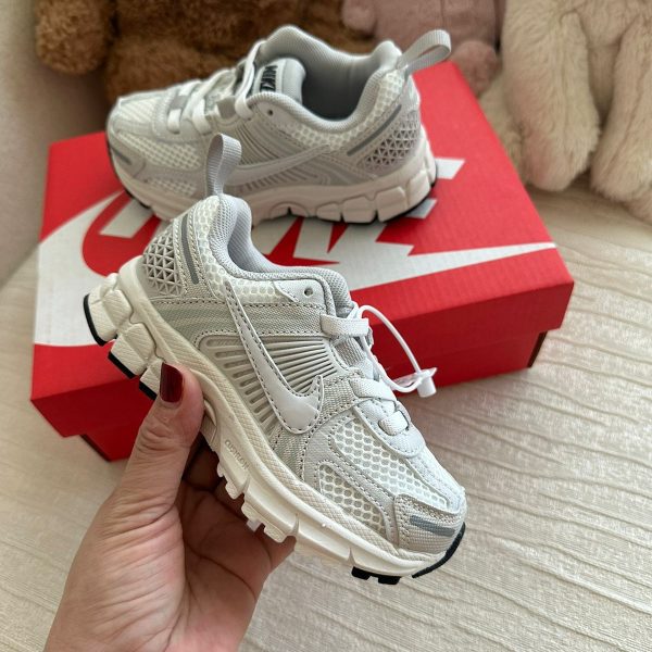 White Nike toddler sneakers with mesh panels resting on a red Nike shoebox, plush toys in the background.