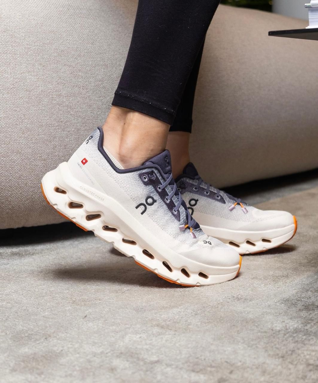 WhatsApp_Image_2025-01-22_at_13.03.38 | UAE SPORT STORE Light gray On running shoes with thick white soles and orange tips, worn by a person in black leggings on a carpeted floor.