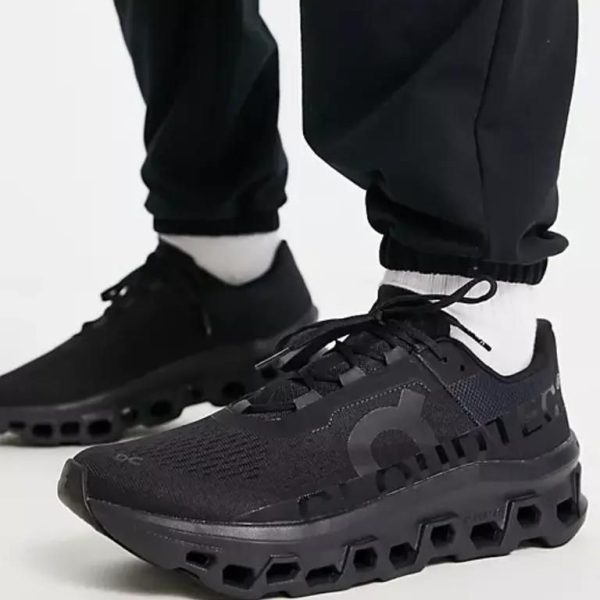 Close-up of black athletic sneakers with a chunky hollow lattice sole, worn with white socks and black joggers in a side view.