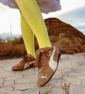 Person in bright yellow tights wears brown Puma sneakers on cracked dry ground outdoors.