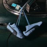 Light blue Puma sneakers hanging by their laces from a vintage dark-green car door.