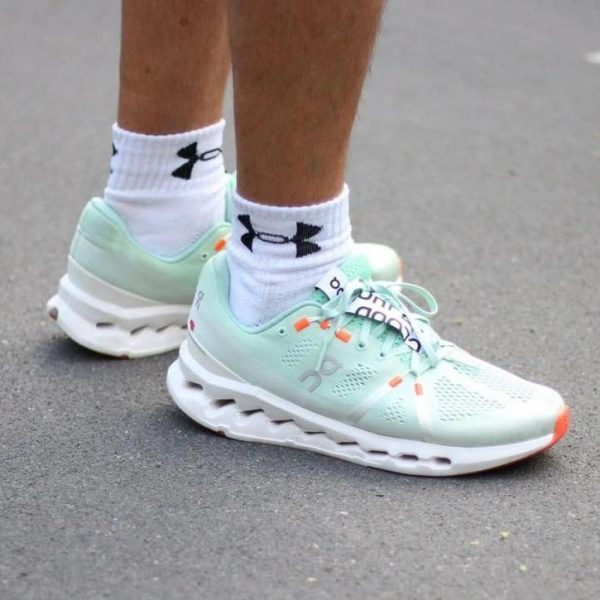 Mint-green running shoes with a thick white sole, laced and worn with white Under Armour socks on a paved surface.