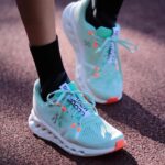 Teal running shoes with white soles on a track, laces tied, close-up of feet in black socks.