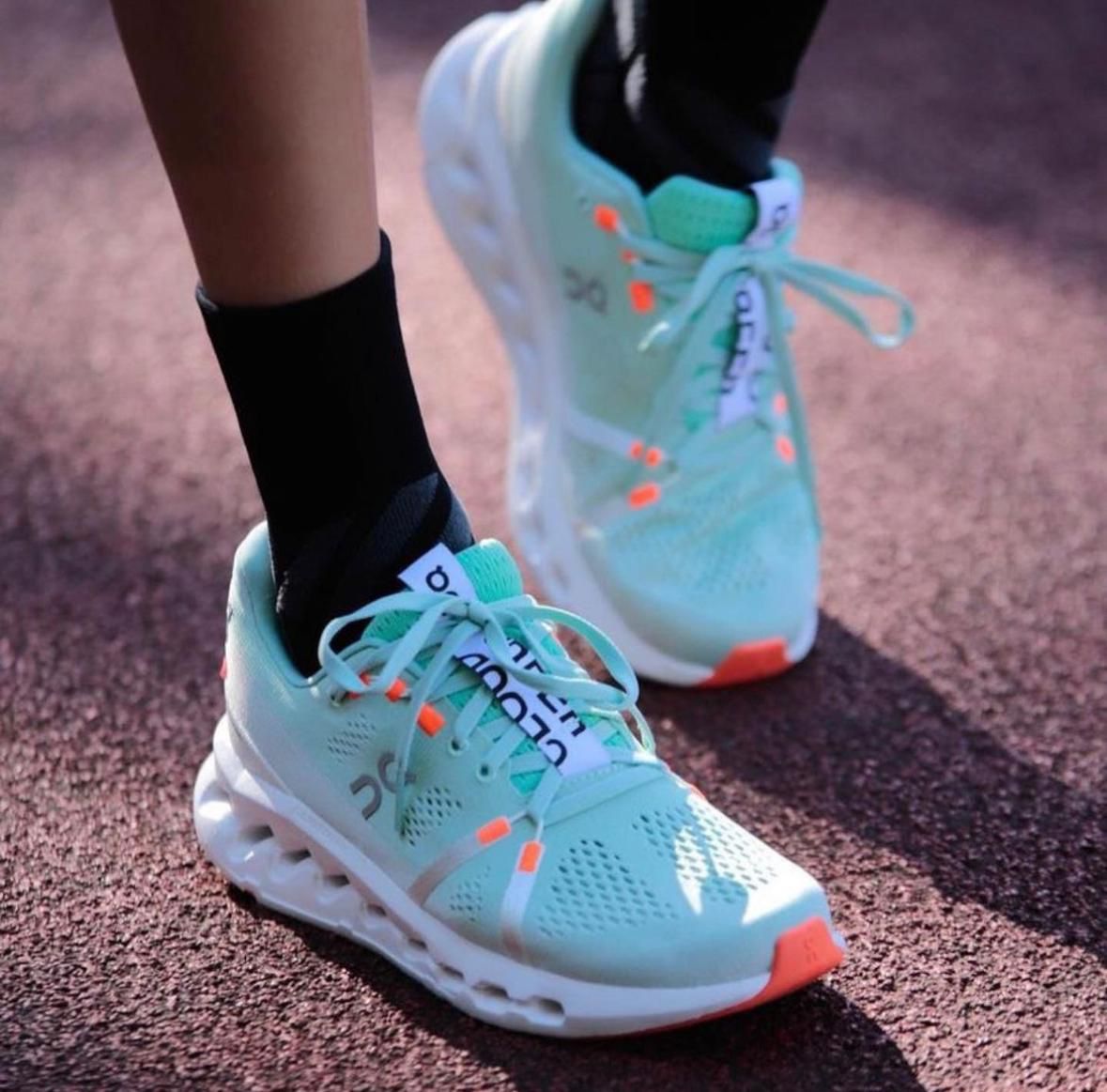 WhatsApp_Image_2025-02-03_at_11.53.44 Teal running shoes with white soles on a track, laces tied, close-up of feet in black socks.