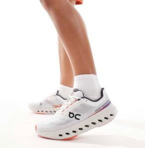 White athletic running shoes with breathable mesh, orange accents and a cushioned sole, worn with white socks.