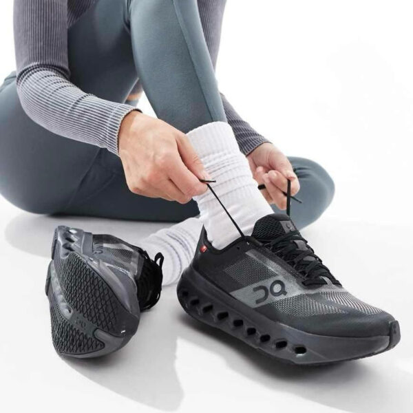 Person seated on the floor tying the laces of black athletic shoes with white socks showing beneath the knees.