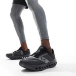 Close-up of a person wearing black and gray On running shoes with cloud-like outsole pods on a white background.