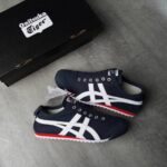 WhatsApp_Image_2025-02-11_at_17.14.29 | UAE SPORT STORE Pair of navy blue Onitsuka Tiger sneakers with white stripes and red sole, placed beside a black Onitsuka Tiger shoebox on a gray surface, tag still attached.