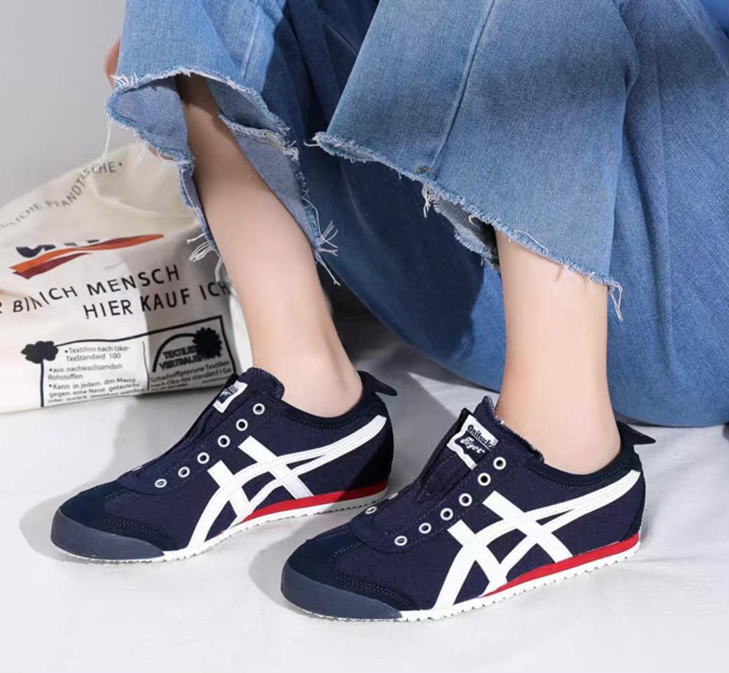 WhatsApp_Image_2025-02-11_at_17.15.37 | UAE SPORT STORE Navy blue sneakers with white cross stripes and a red accent along the midsole, worn by a person in frayed-hem jeans, on a light floor with a printed bag in the background.