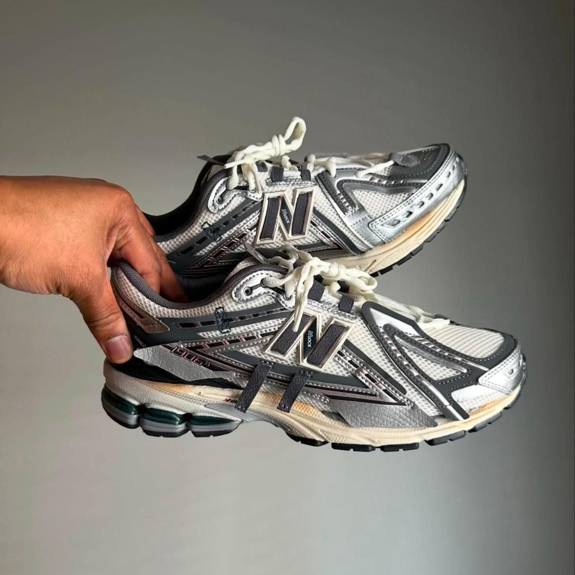 WhatsApp_Image_2025-02-12_at_11.07.52 | UAE SPORT STORE Hand holding a pair of gray and white New Balance running shoes with white laces and black accents