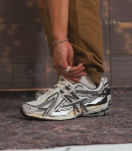 WhatsApp_Image_2025-02-12_at_11.08.01 | UAE SPORT STORE Person tying the laces of a white and gray running shoe, wearing brown pants and a silver bracelet on the wrist