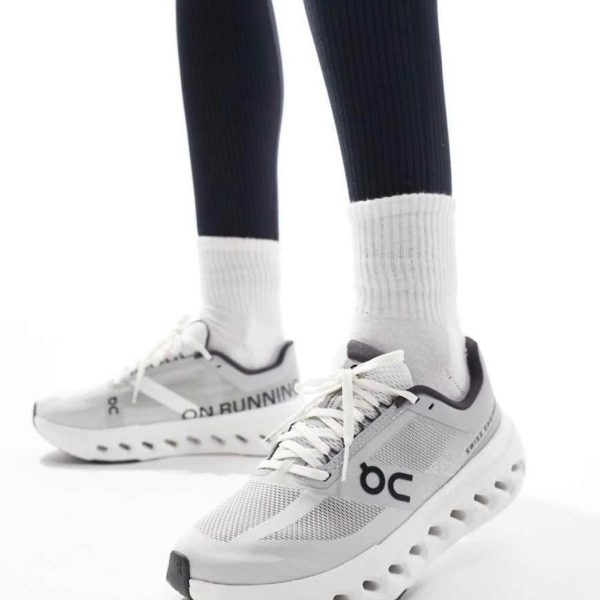 White On Running running shoes on a person wearing white socks and dark athletic leggings; sneakers have a chunky perforated sole and mesh upper.