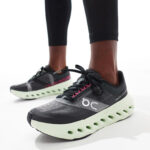Close-up of black and gray running shoes with a lime-green cushioned sole, worn by someone in black leggings.