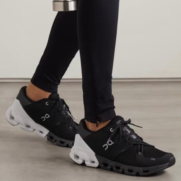 Close-up of black and white On running shoes on a person’s feet indoors; black upper, chunky white sole, logo visible on side.