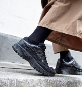 Close-up of black athletic sneakers stepping onto a curb, with a beige coat visible overhead.