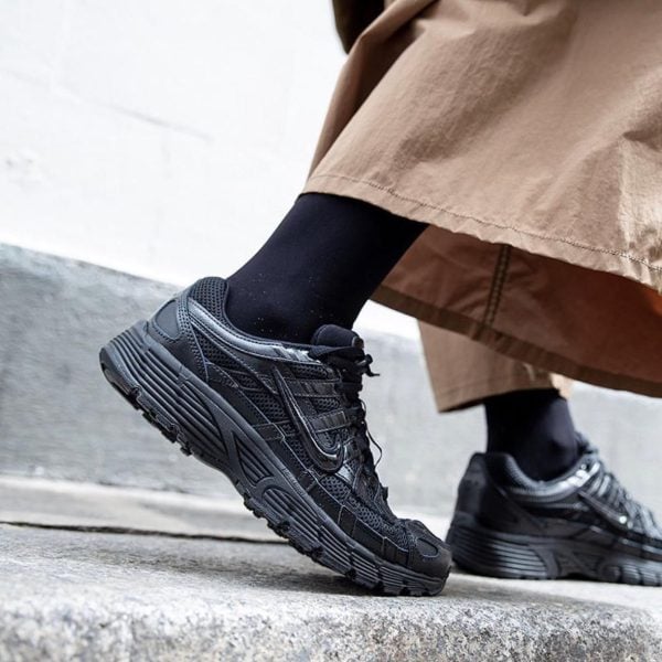 Close-up of black athletic sneakers stepping onto a curb, with a beige coat visible overhead.