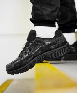 Black athletic sneaker with a chunky sole stepping over a yellow curb, white sock visible above the shoe edge.