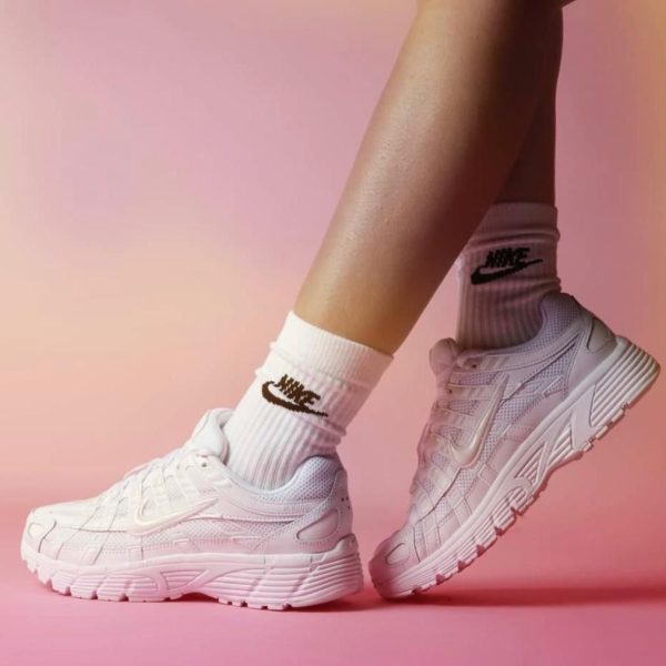 Close-up of white Nike running shoes worn with white socks, standing on a pink surface.