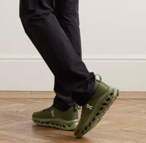 WhatsApp_Image_2025-02-18_at_10.49.56 | UAE SPORT STORE Person wearing olive green On running shoes stepping forward on a wooden floor.
