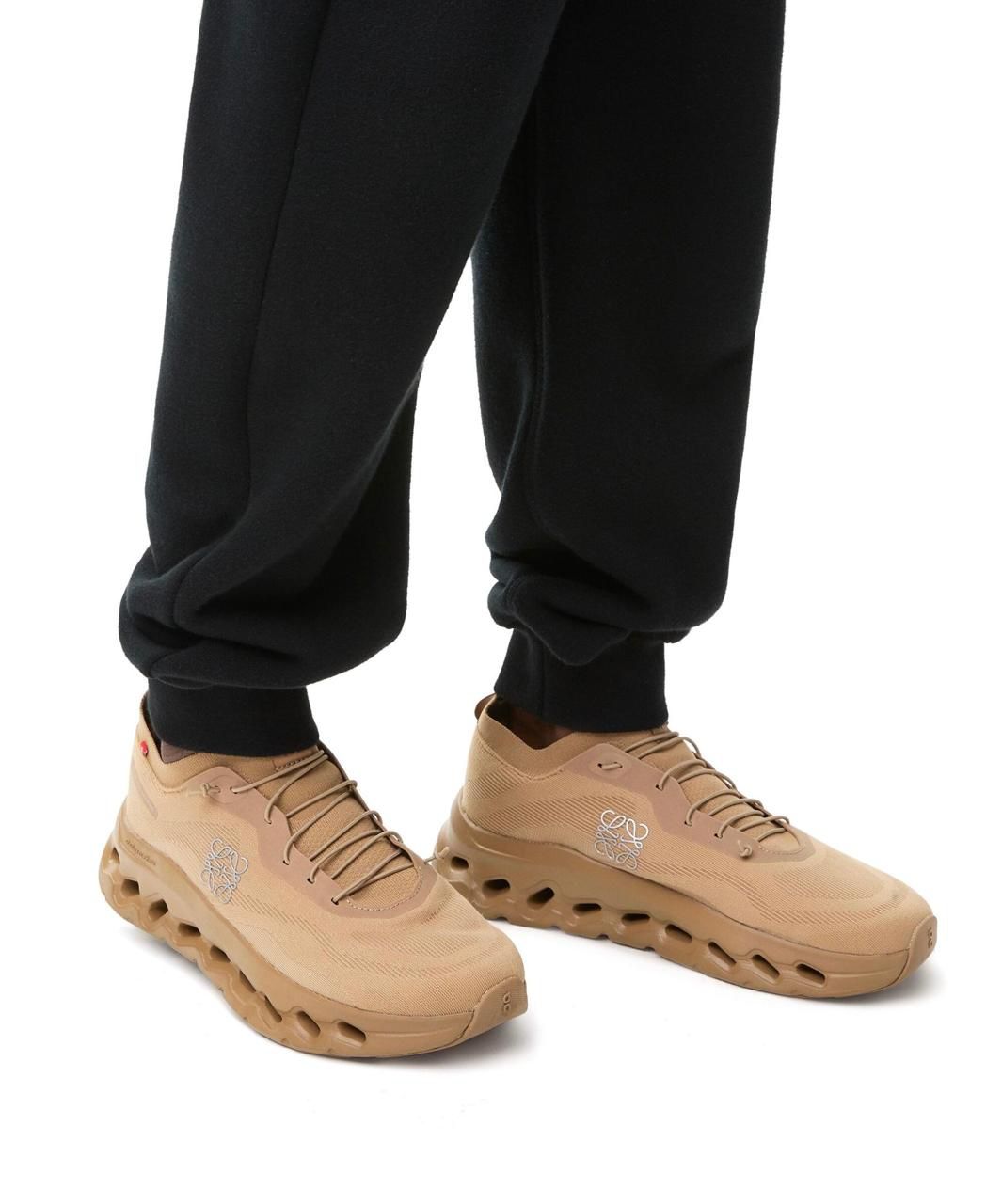 WhatsApp_Image_2025-02-18_at_12.07.04 | UAE SPORT STORE Beige athletic sneakers with a chunky hollow sole worn with black joggers/A pair of tan sneakers with cut-out sole on a model wearing black sweatpants.
