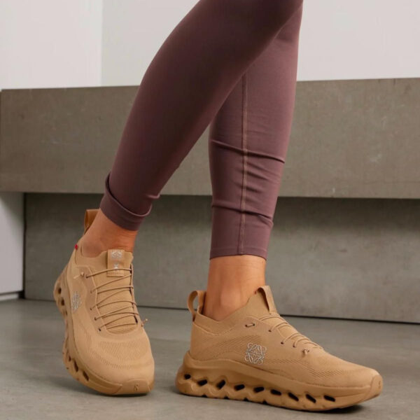 Person wearing tan athletic sneakers with mauve leggings, standing on a concrete floor.