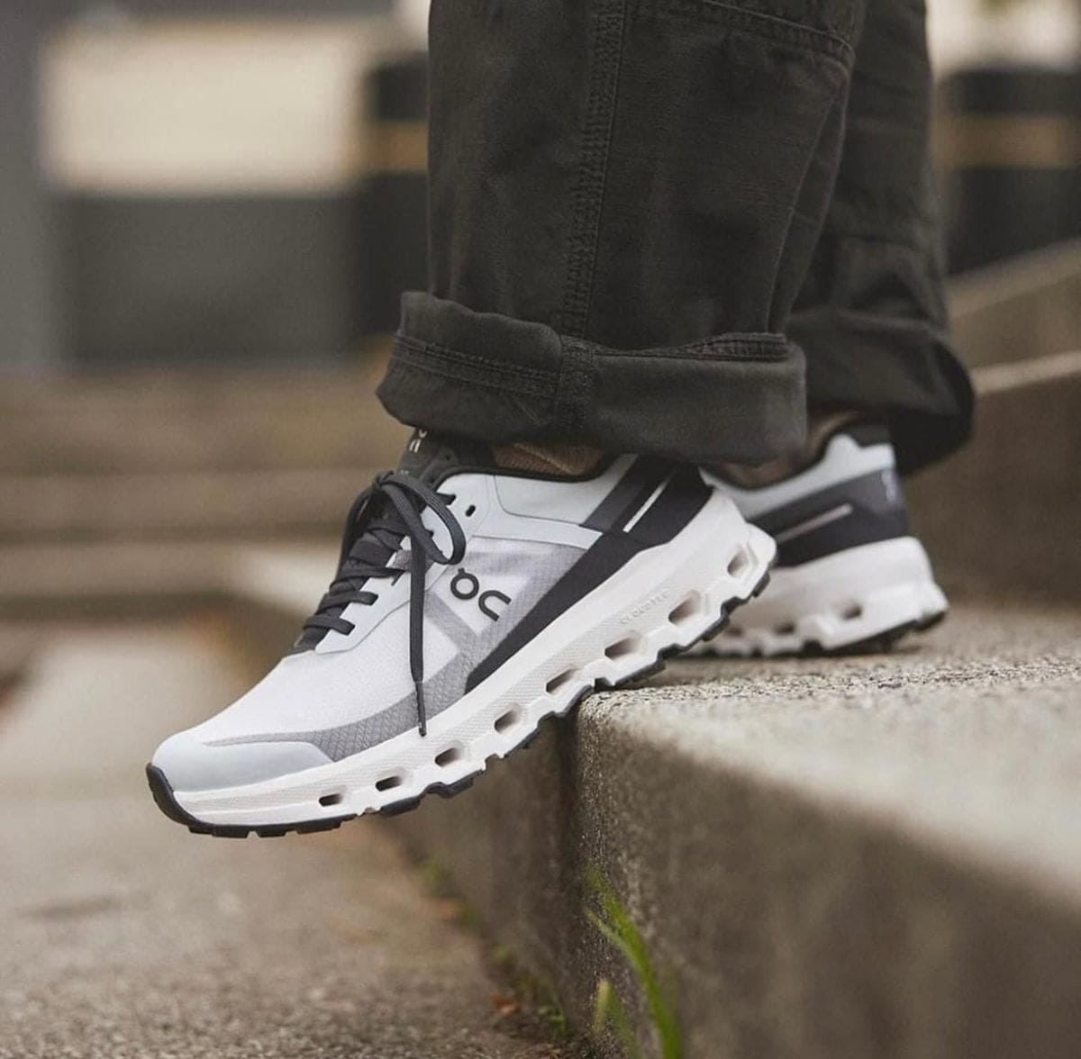 White and gray athletic sneakers stepping onto a concrete curb, rolled dark jeans visible at the ankle