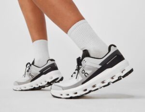 White and gray running shoes on feet wearing white crew socks, shown in a side stance on a light background.