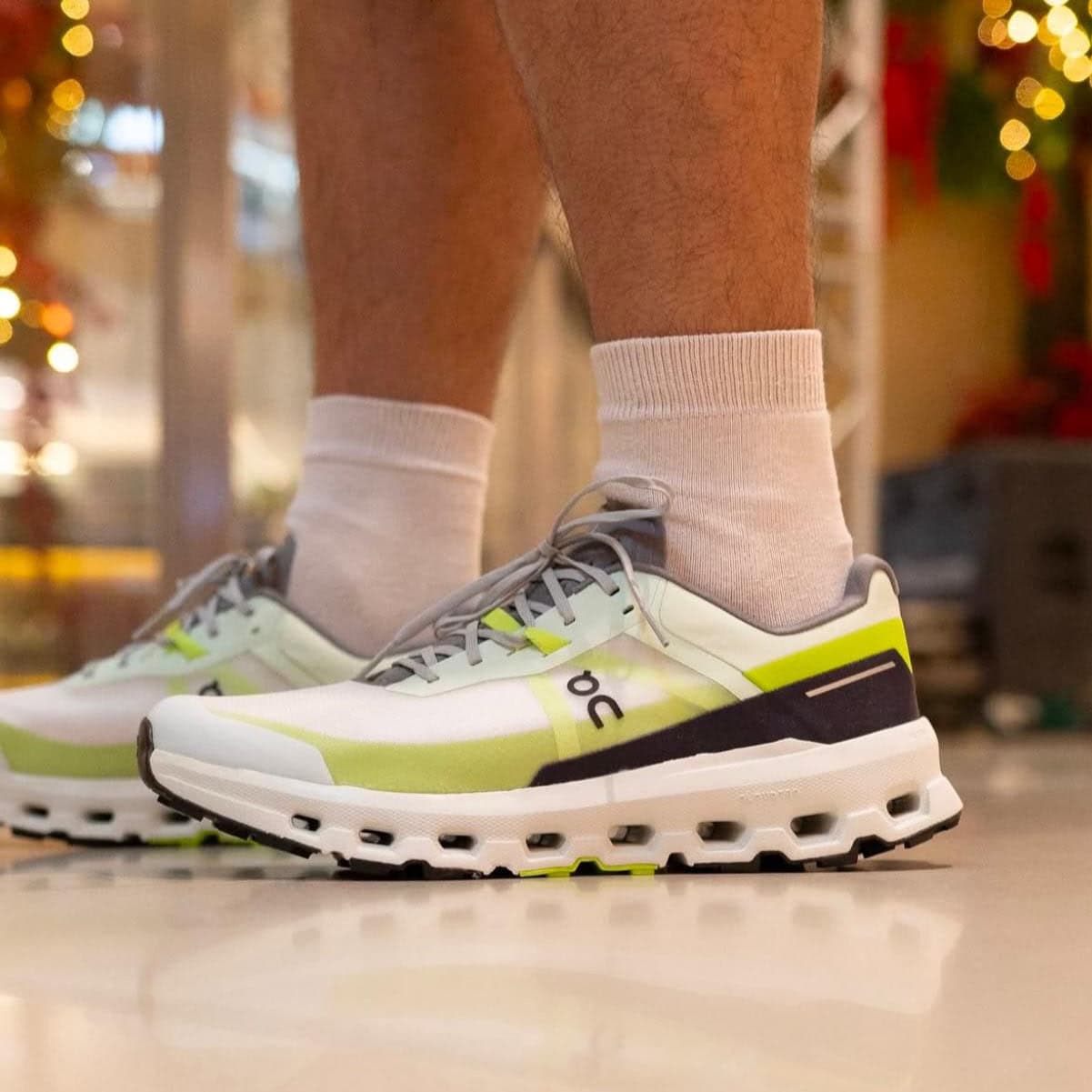 WhatsApp_Image_2025-02-22_at_11.32.38 | UAE SPORT STORE Close-up of white and lime-green running shoes with gray laces, worn with light gray socks.