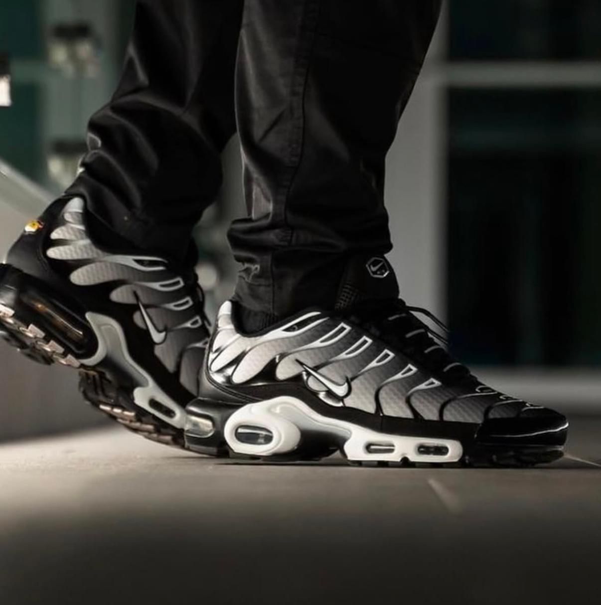 WhatsApp_Image_2025-02-24_at_12.27.31 | UAE SPORT STORE Black and white athletic sneakers with visible air-cushion soles, worn by a person standing indoors on a smooth surface.