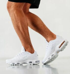 WhatsApp_Image_2025-02-24_at_16.04.48 | UAE SPORT STORE Person wearing white Nike sneakers mid-step, feet angled on a reflective white floor against a light background. Tattooed legs visible.
