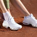 Person tying white athletic sneakers on a dusty red track, white socks visible near ankles
