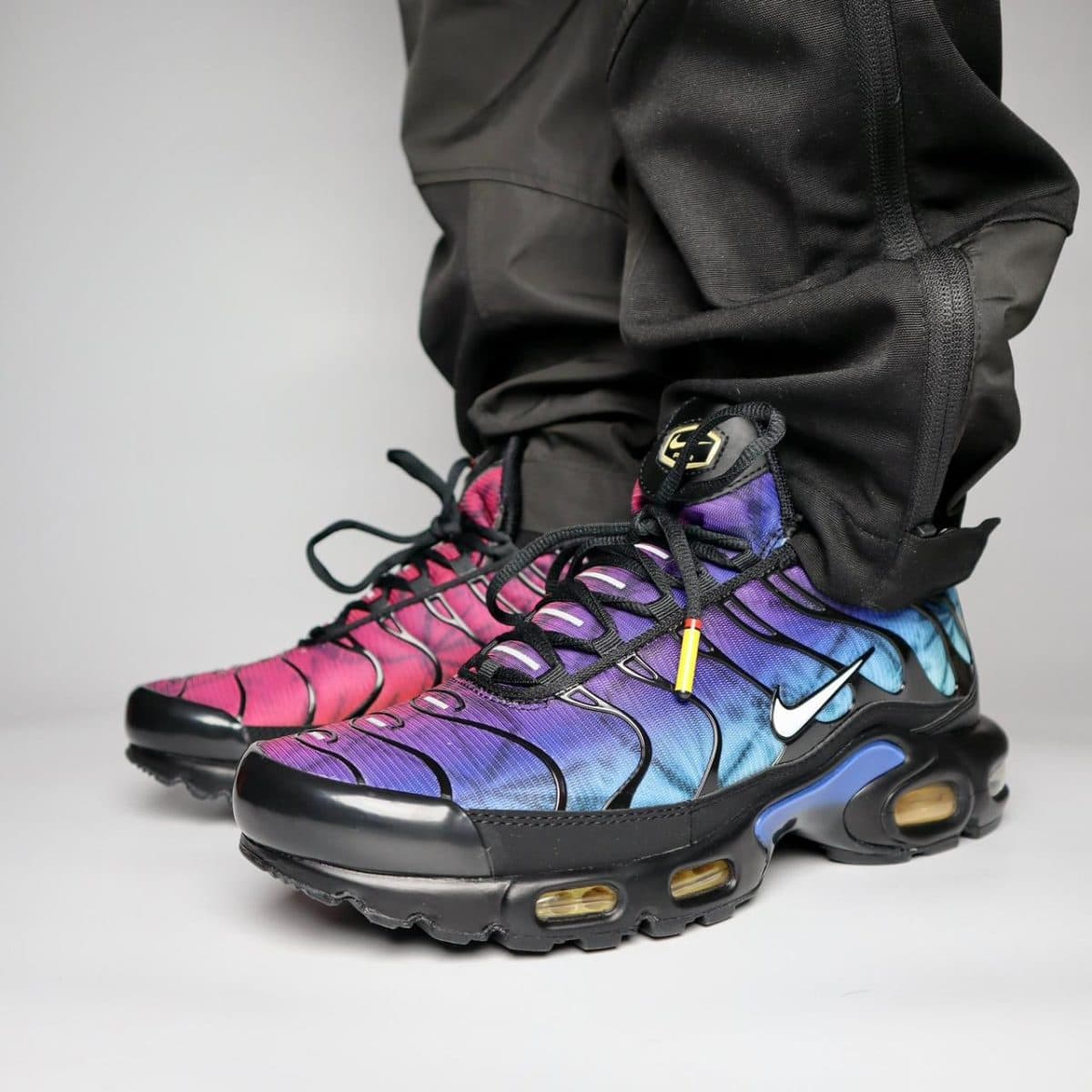 Close-up of gradient Nike sneakers in pink, purple, and blue worn with black pants.