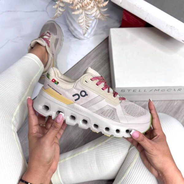 Beige and white running shoe with pink laces held by a person, showing a chunky sole and On logo; Stella McCartney box in the background.