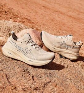 Beige ASICS running shoes resting on sandy, rocky desert terrain.
