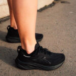 Person wearing black running shoes standing on pavement; close-up of shoes and ankles outdoors