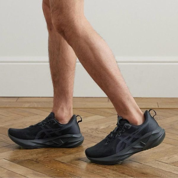 Person walking indoors in black athletic shoes on a wooden floor, mid-step