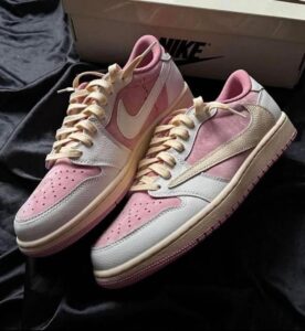 Pink and white Nike sneakers with beige laces resting on black fabric, a box in the background.