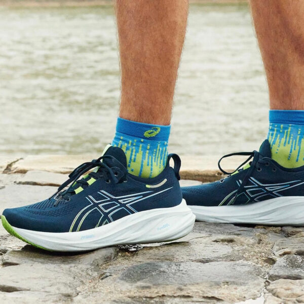 Navy blue running shoes with white soles and neon accents on a rocky lakeside, bright patterned socks visible.