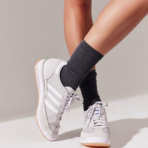 Two legs wearing light gray sneakers and dark gray socks, one foot crossed over the other.