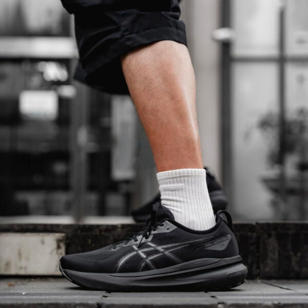 Person wearing black running shoes and white socks stepping onto a curb in an urban setting, focus on footwear.