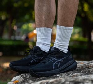 Close-up of a person wearing black running shoes and white socks standing on a rock outdoors.